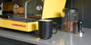 A black Ember Mug² sits on a gray countertop next to a yellow La Marzocco espresso machine.