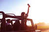 Man driving Jeep while women in passenger seat stands and holds Ember Travel Mug to the sky.