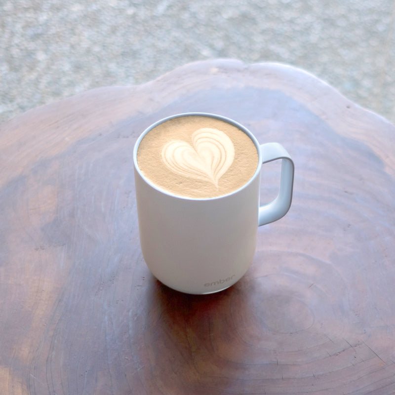 Latte heart in a white Ember Mug on a dark wooden table.