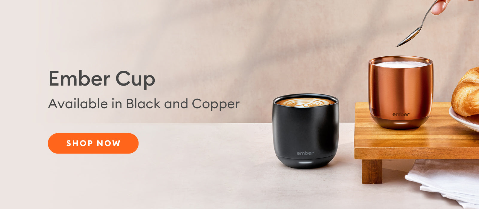 Two Ember Cups in black and copper on a countertop with a croissant sitting nearby.