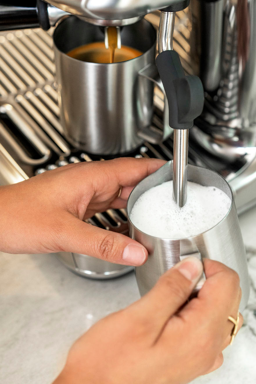 Upclose image of a hand steaming milk using a espresso machine with Ember mug in the background.